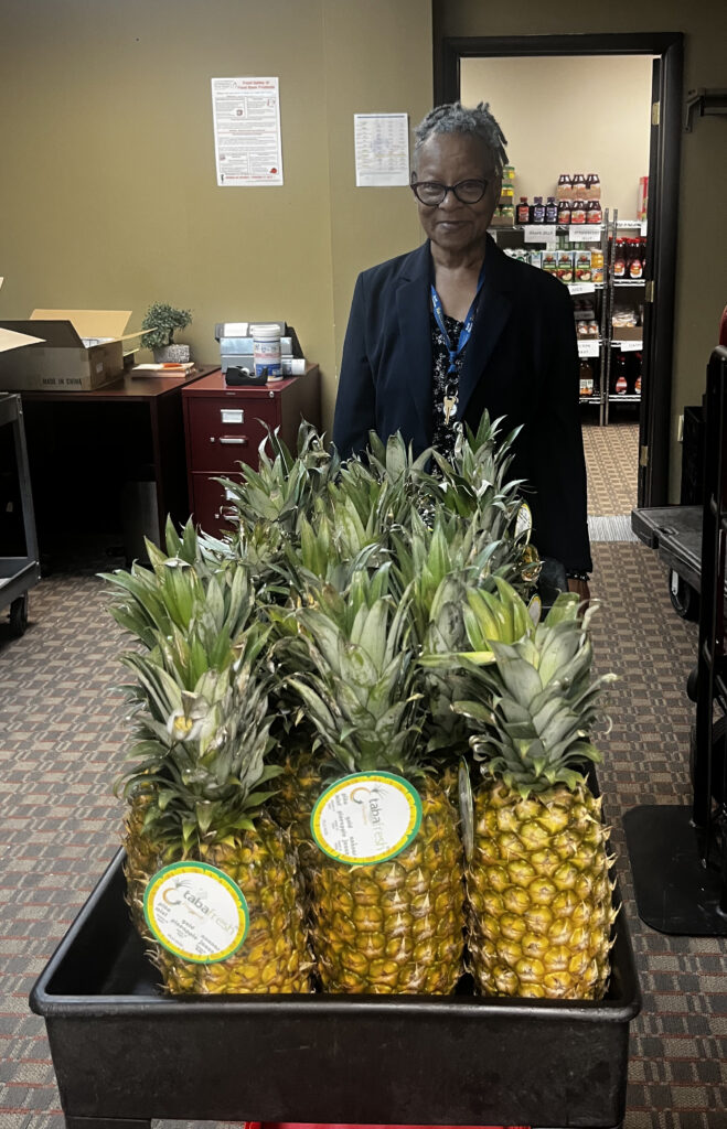 A staff member standing behind a cart full of whole pineapples.