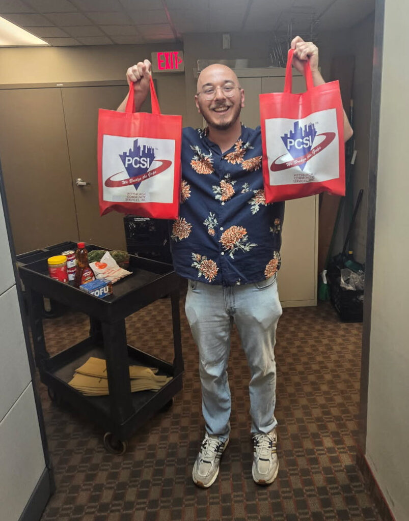 Julian holds up two PCSI tote bags for food pantry groceries